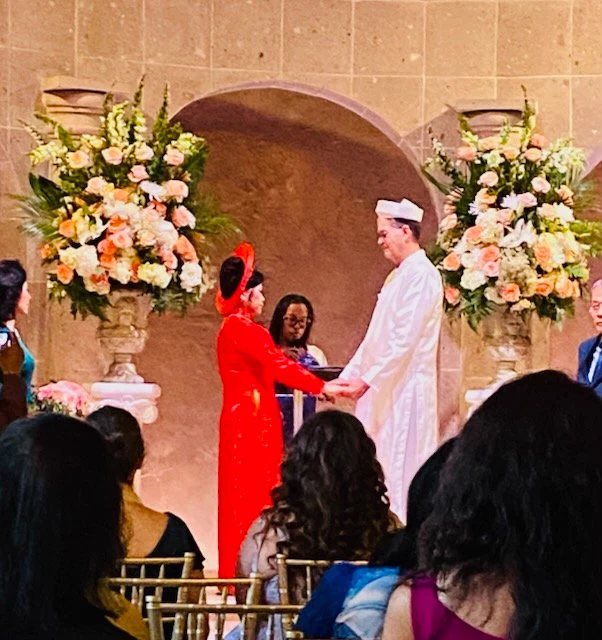 A bride and groom in traditional Vietnamese wedding attire holding hands as Hong Tam officiates their ceremony