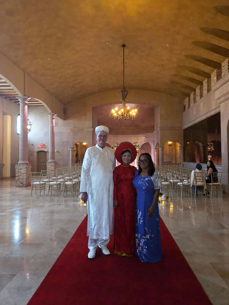 A couple in traditional Vietnamese wedding attire standing with officiant Hong Tam in their ceremony venue